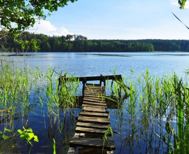 Pomost nad jeziorem w Giżycku - Drewniany pomost prowadzący w głąb jeziora otoczonego trzcinami, idealne miejsce na wypoczynek w okolicach Giżycka.